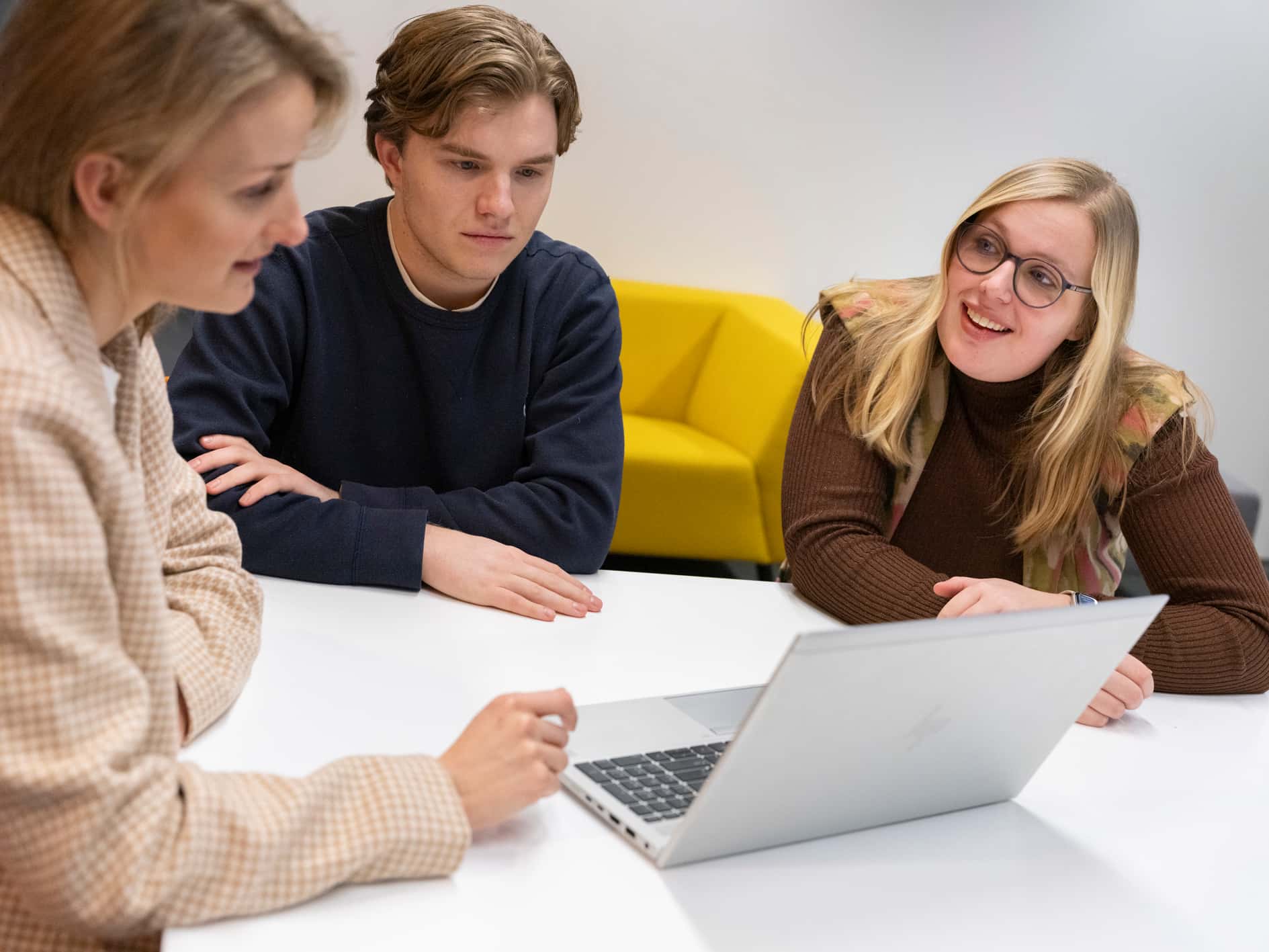 Twee jonge talenten zitten aan tafel met een hr-professional, achter één laptop.