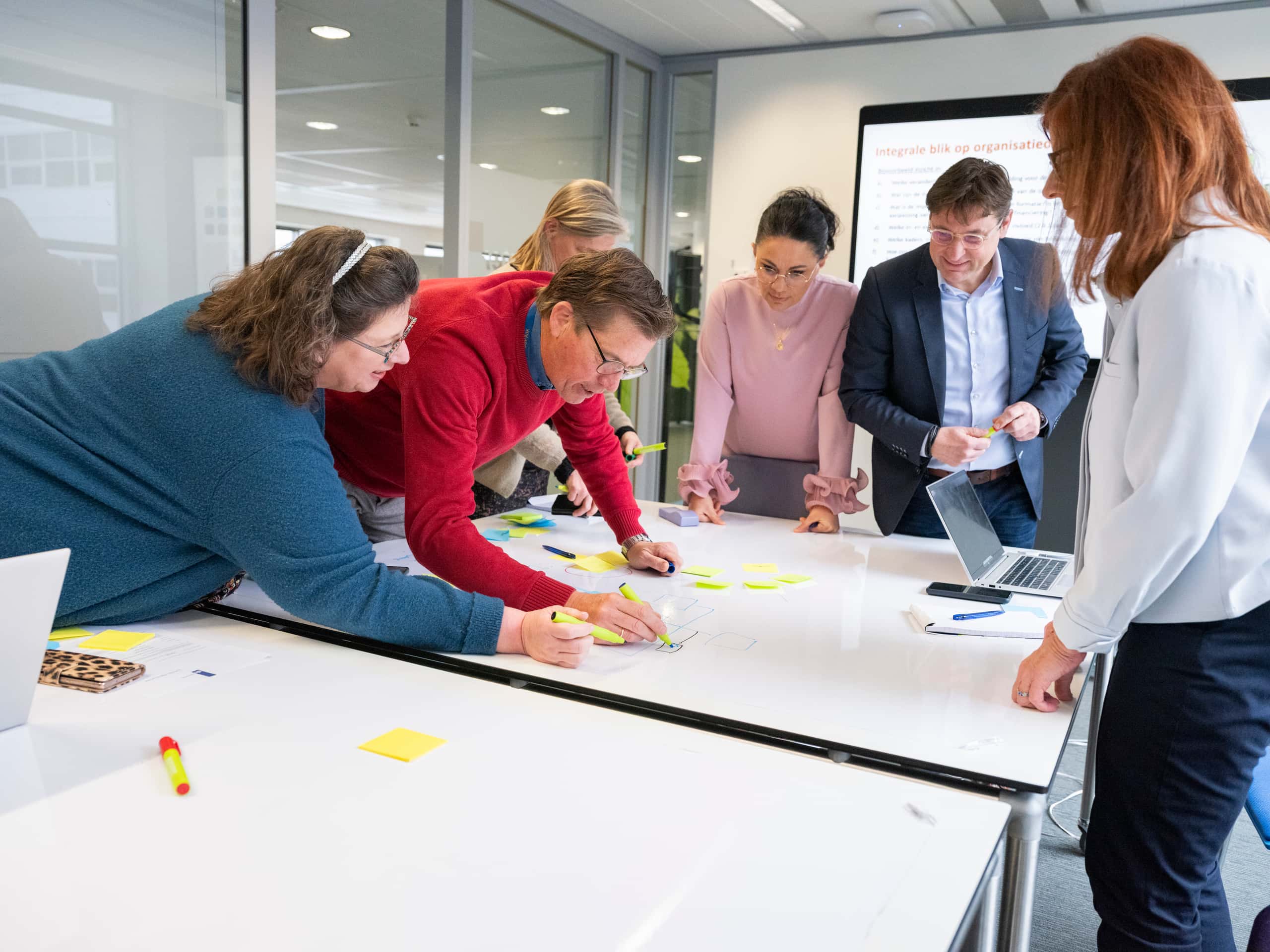 Meerdere medewerkers staan voorover gebogen over een tafel