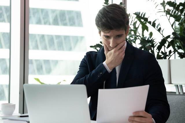 Bezorgd kijkende man met laptop en dossiers